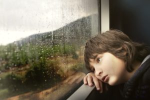 窓から雨の様子を見る少年